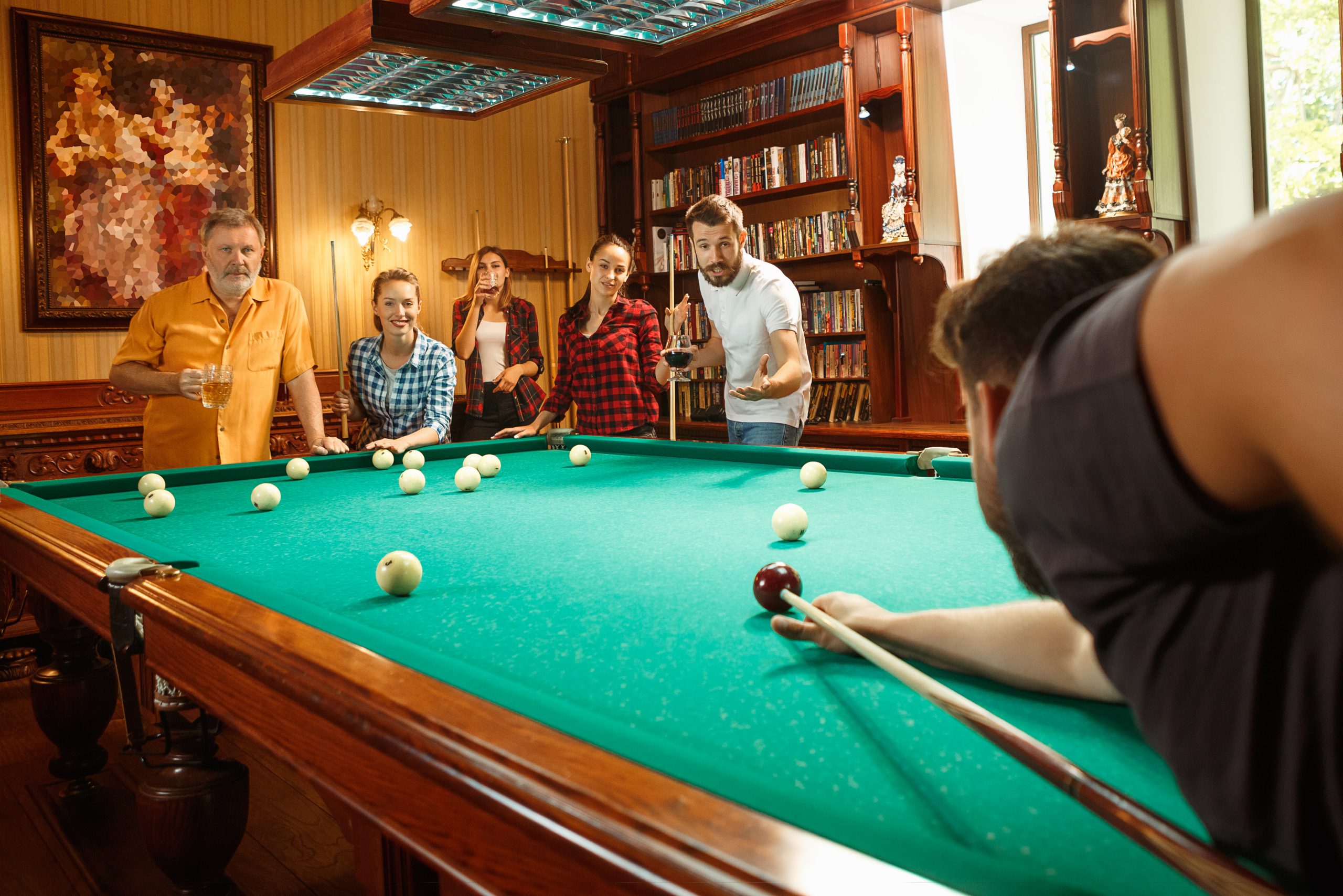 Young smiling men and women playing billiards at office or home after work. Business colleagues involving in recreational activity. Friendship, leisure activity, game concept. Human emotions concepts
